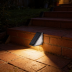 Wedge-shaped solar step light fixed to a brick garden step riser, casting a warm white wash across the tread below at night