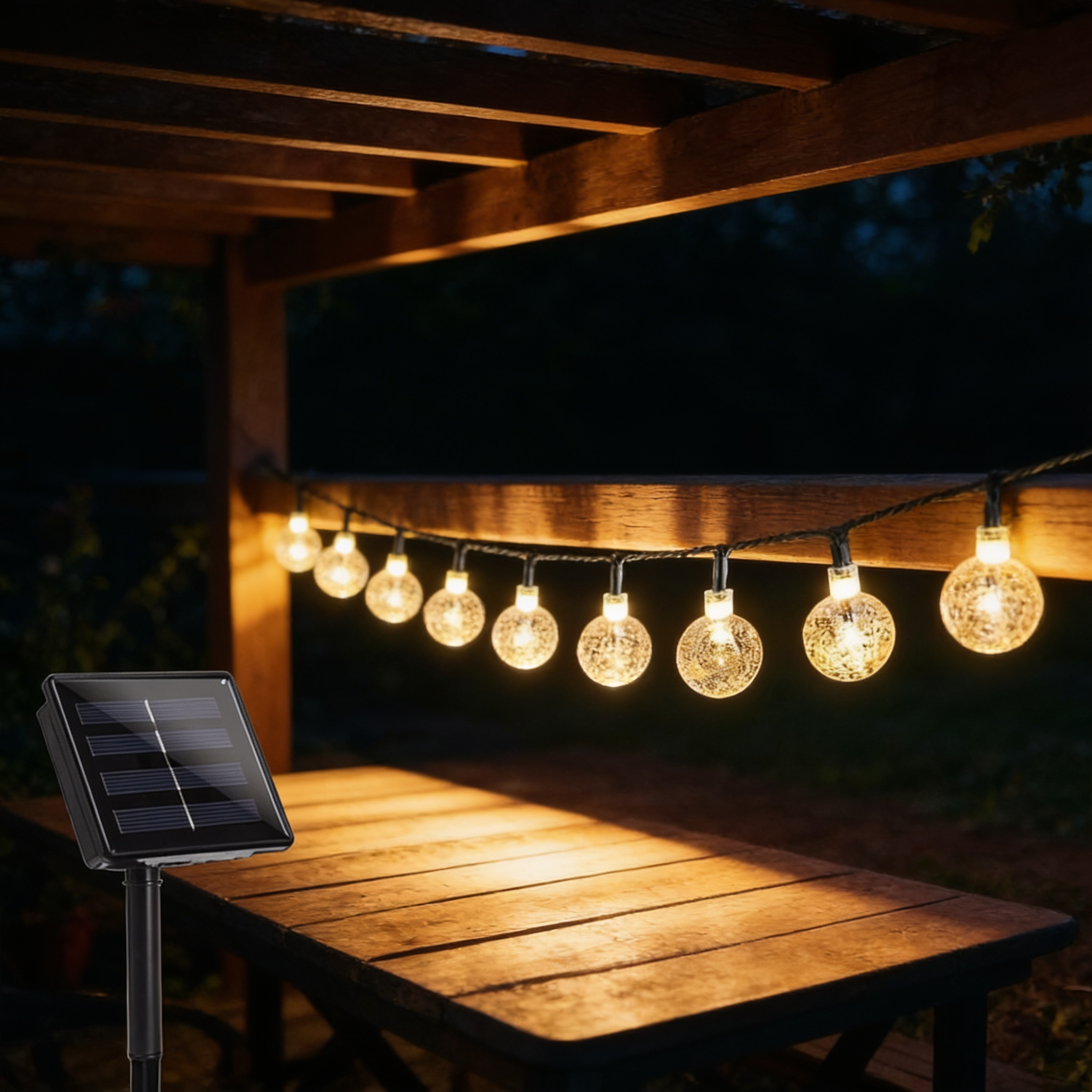 Solar crystal globe string lights strung along a garden pergola rail above a wooden table, warm white bulbs glowing at night