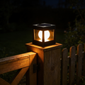 Square black solar post cap light with a glowing frosted globe inside, sitting on top of a wooden garden gate post at night