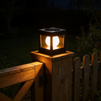 Square black solar post cap light with a glowing frosted globe inside, sitting on top of a wooden garden gate post at night