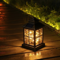 Square Mission-style solar lantern with fairy light wire glowing inside clear glass panes, standing on damp garden decking at night