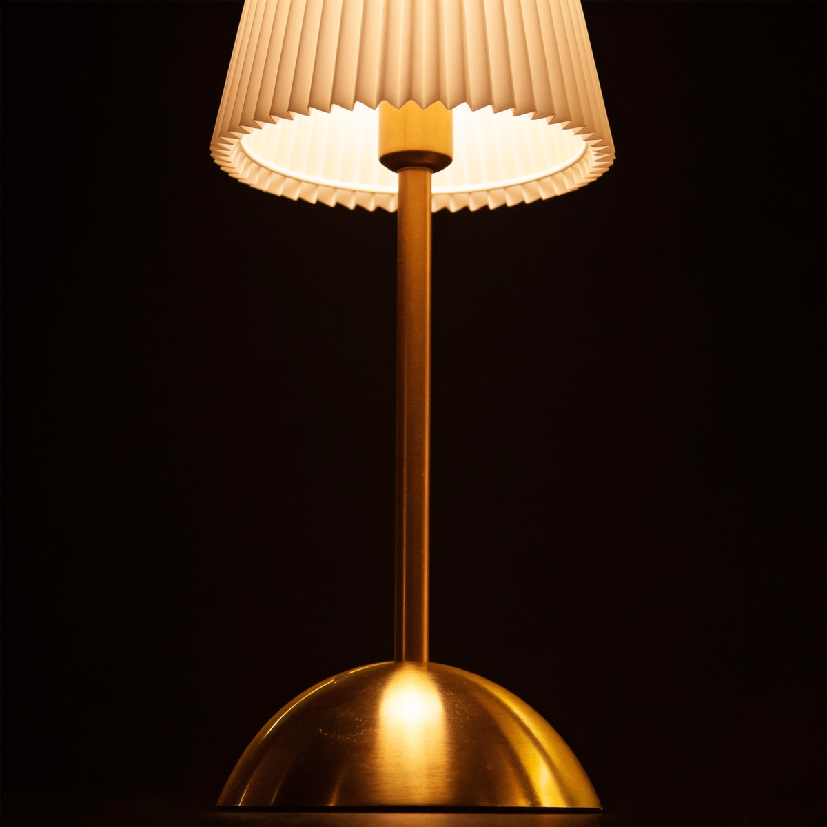Close detail of the spun brass domed base and touch switch of the cordless pleated table lamp