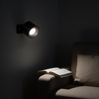 Cordless puck wall light above a reading armchair, neutral white light on an open paperback