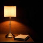The Linen rechargeable table lamp on a dark wooden bedside table at night, its linen drum shade casting a warm pool of light