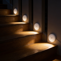 Tread motion sensor stair lights fixed one per riser down a staircase at night, each laying a warm pool of light across the tread below