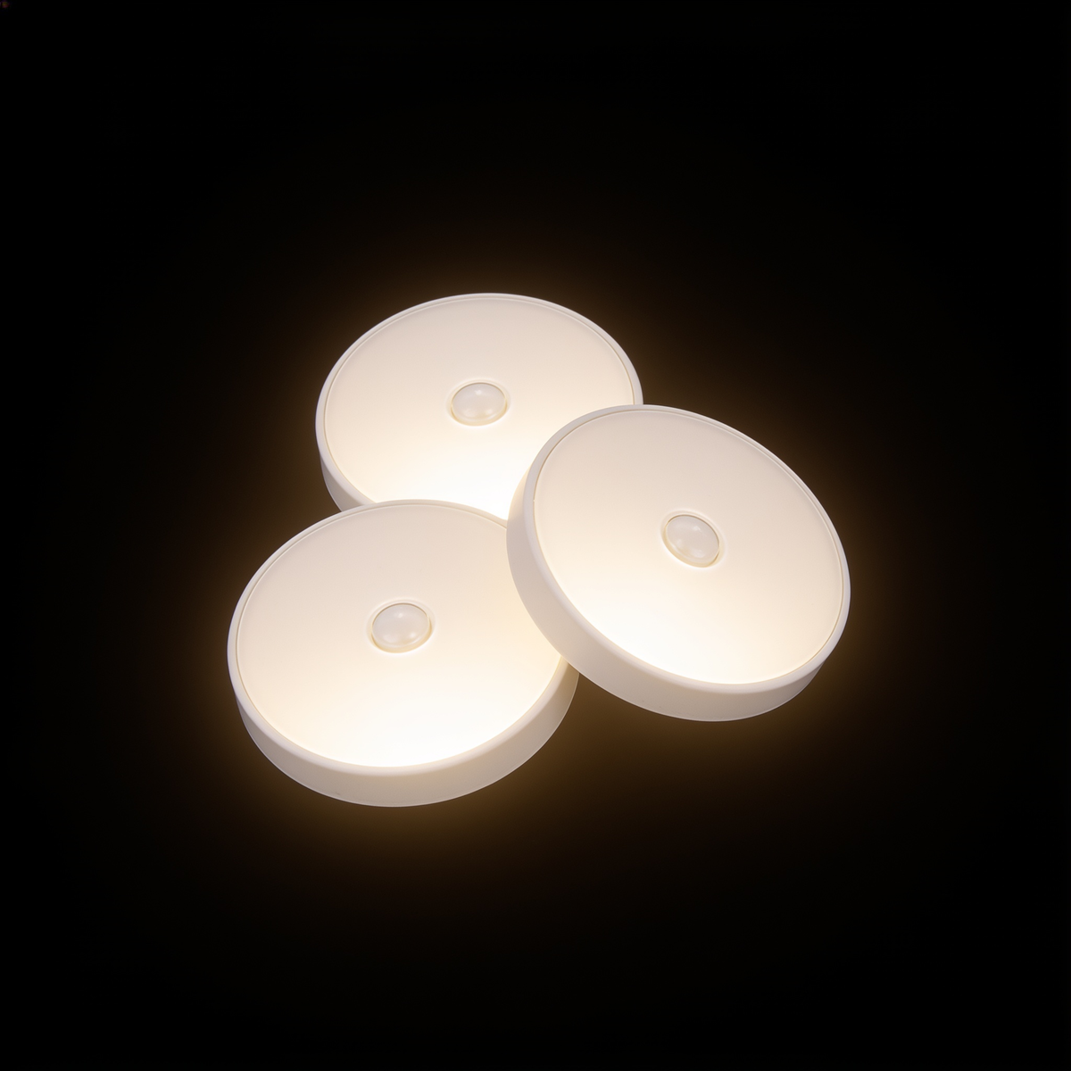 Three Tread motion sensor puck lights grouped on a black studio background