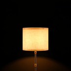 Close view of the Linen table lamp's cream linen drum shade and turned brass stem on a black background