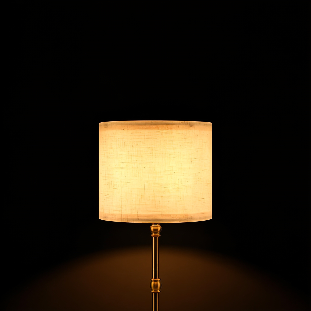 Close view of the Linen table lamp's cream linen drum shade and turned brass stem on a black background